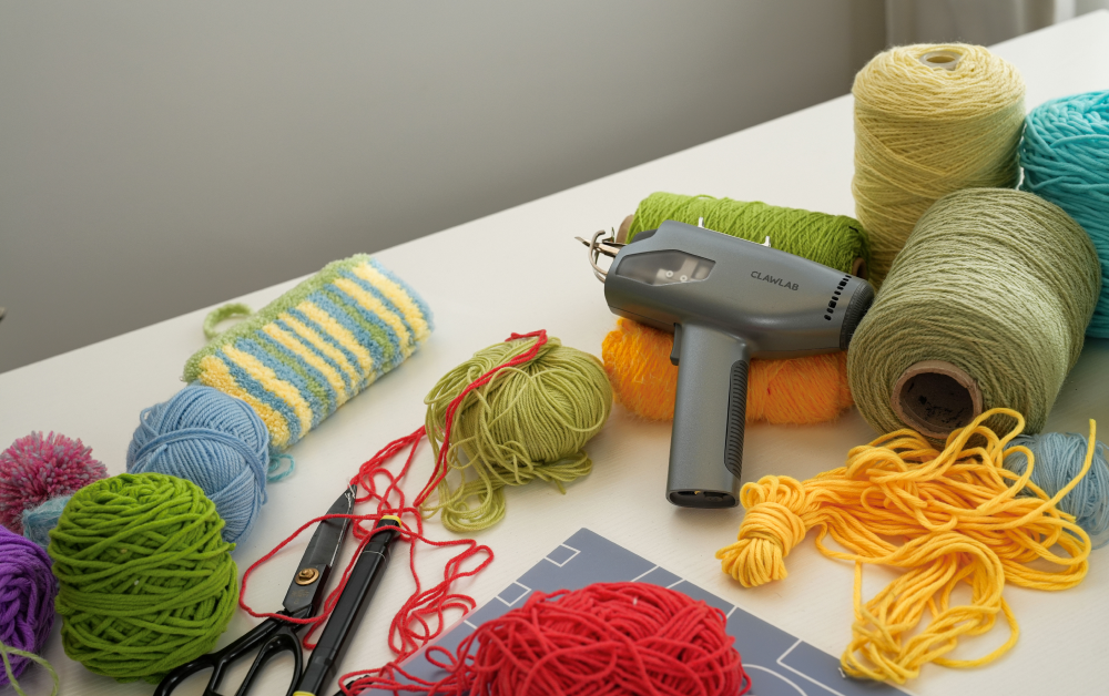 Claw Lab tufting gun on a workspace surrounded by colorful yarn cones, scissors, and essential tufting supplies for custom rug making.