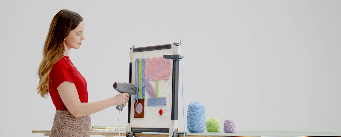 Woman using a Clawlab H1 tufting gun to create a colorful design on a nail-free frame, with pastel yarn nearby.